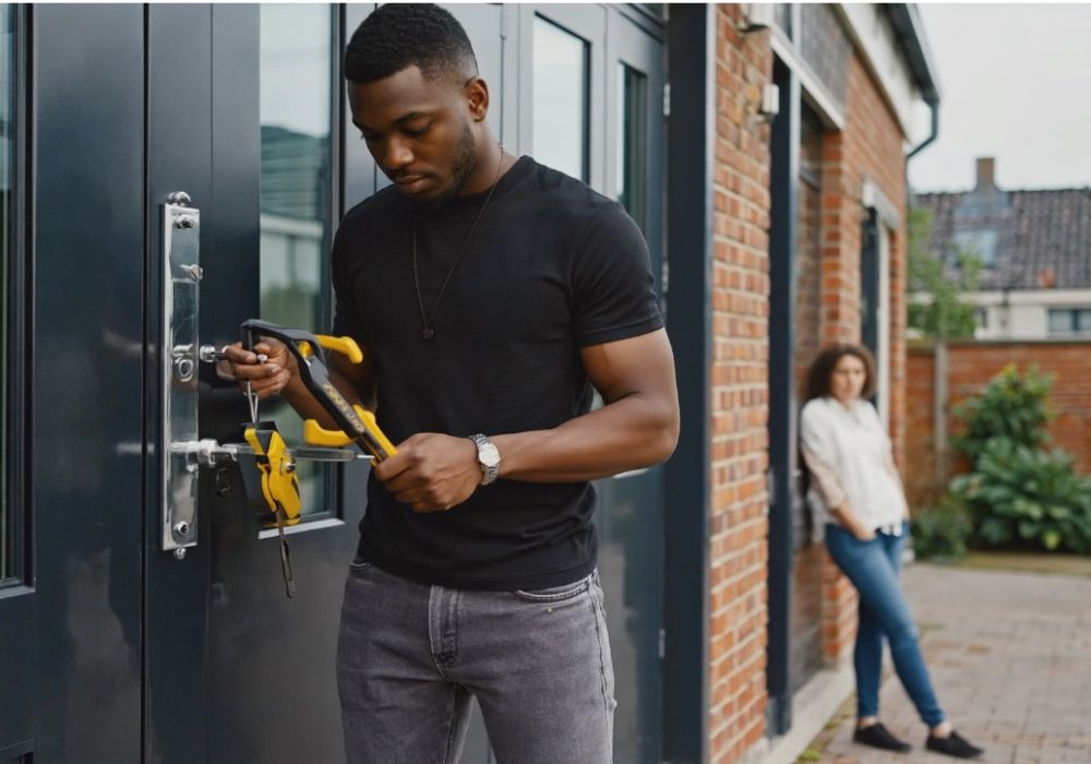 Slotenmaker opent voordeur met professioneel gereedschap terwijl vrouw op achtergrond wacht