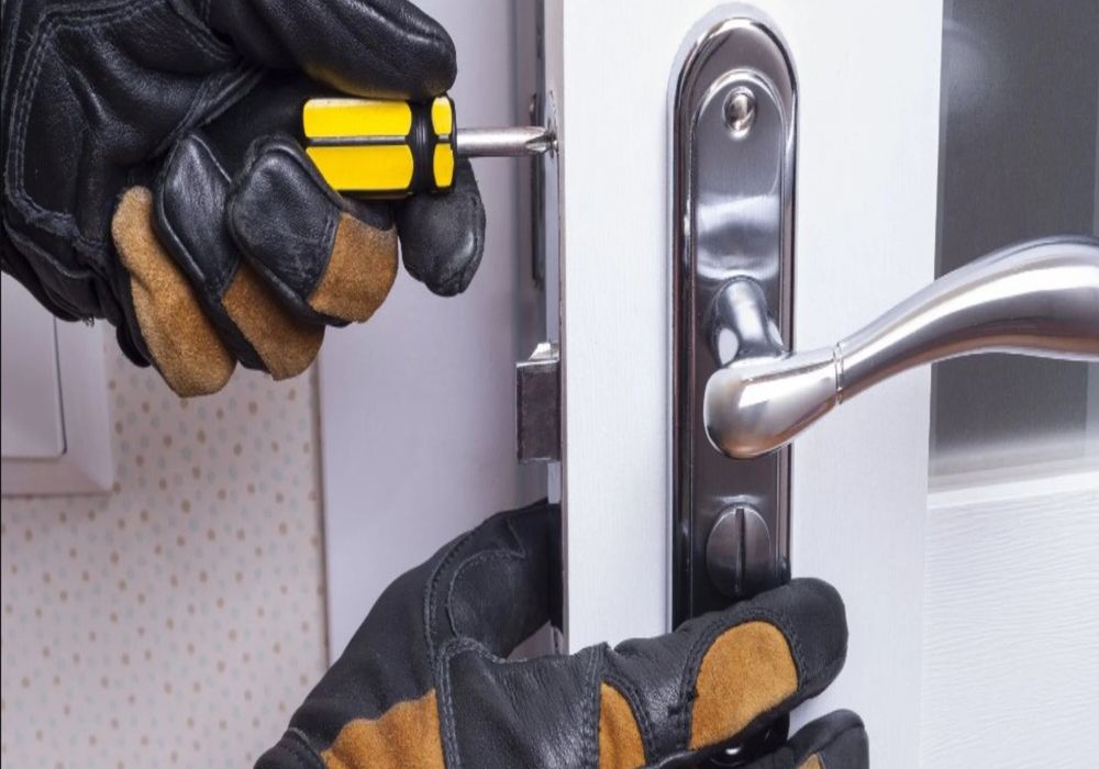 Slotenmaker met handschoenen repareert slot met schroevendraaier.